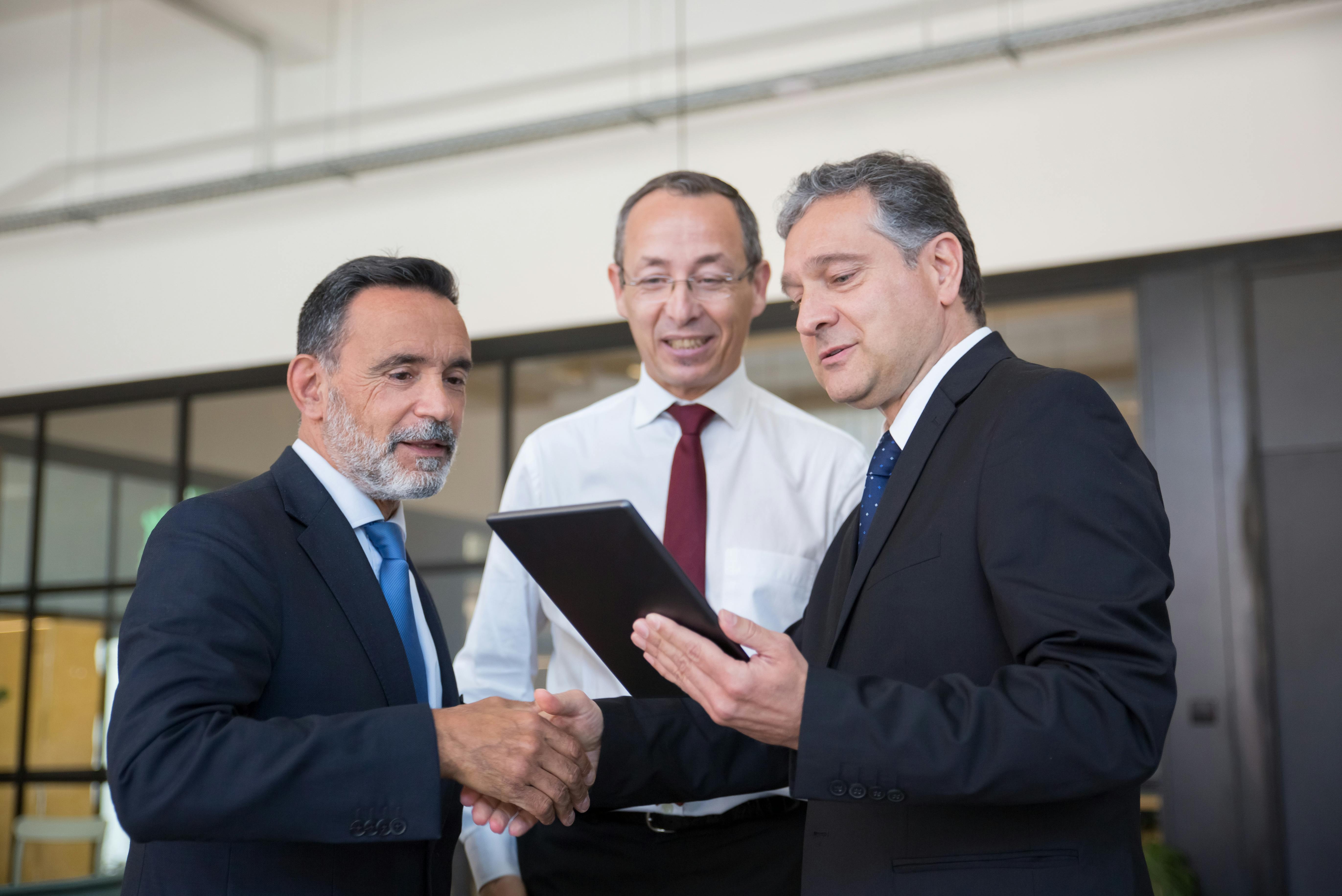 Three businessmen shaking hands and smiling